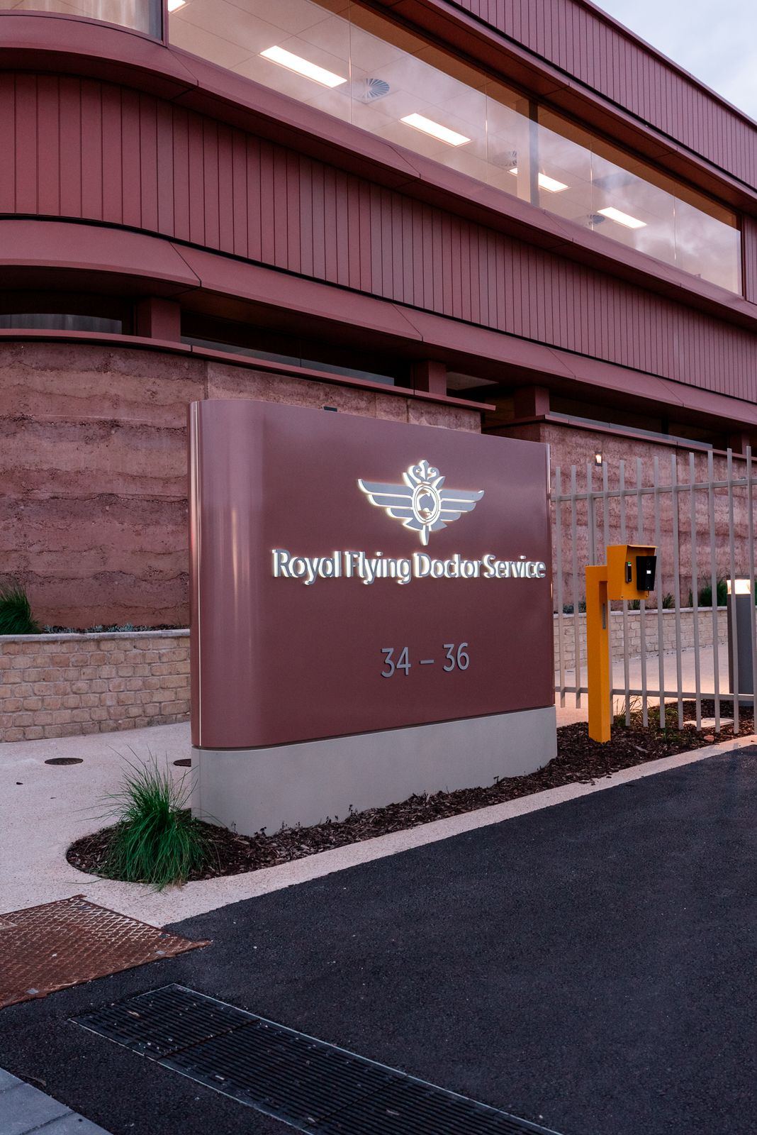 Royal Flying Doctor Service entry sign, rammed-earth wall and a drainage grate in the foreground